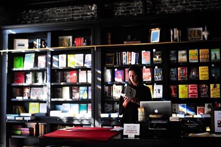 A bookseller reading at the counter of a softly lit bookshop
