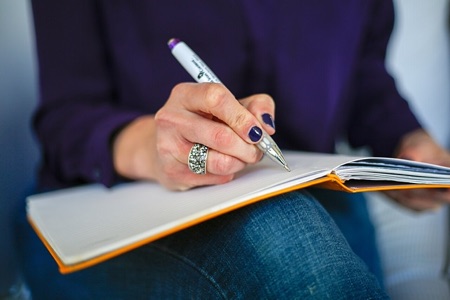 A person writing in a notebook with a pen